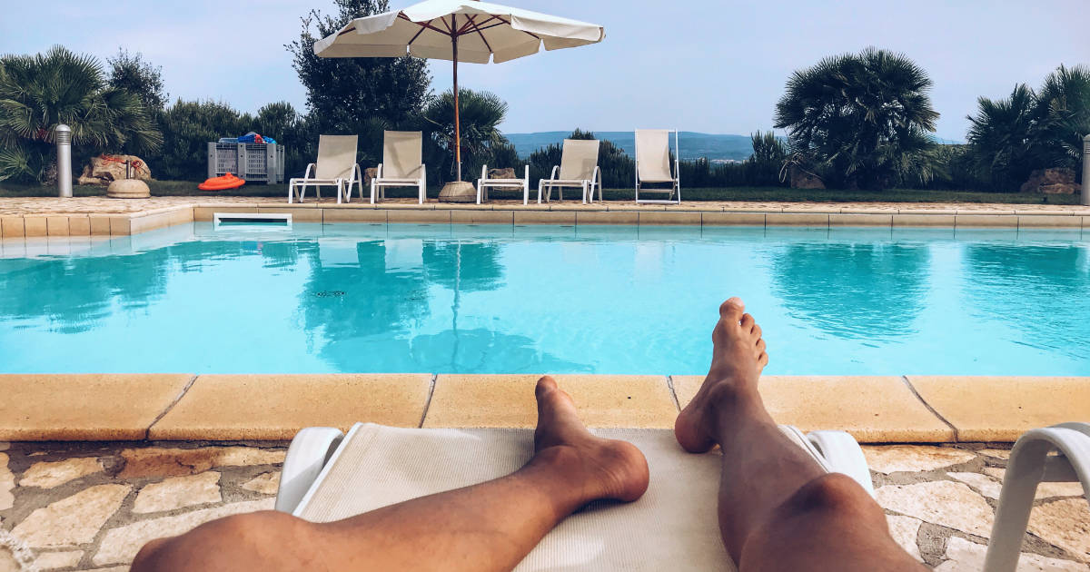 Legs of man relaxing by swimming pool.