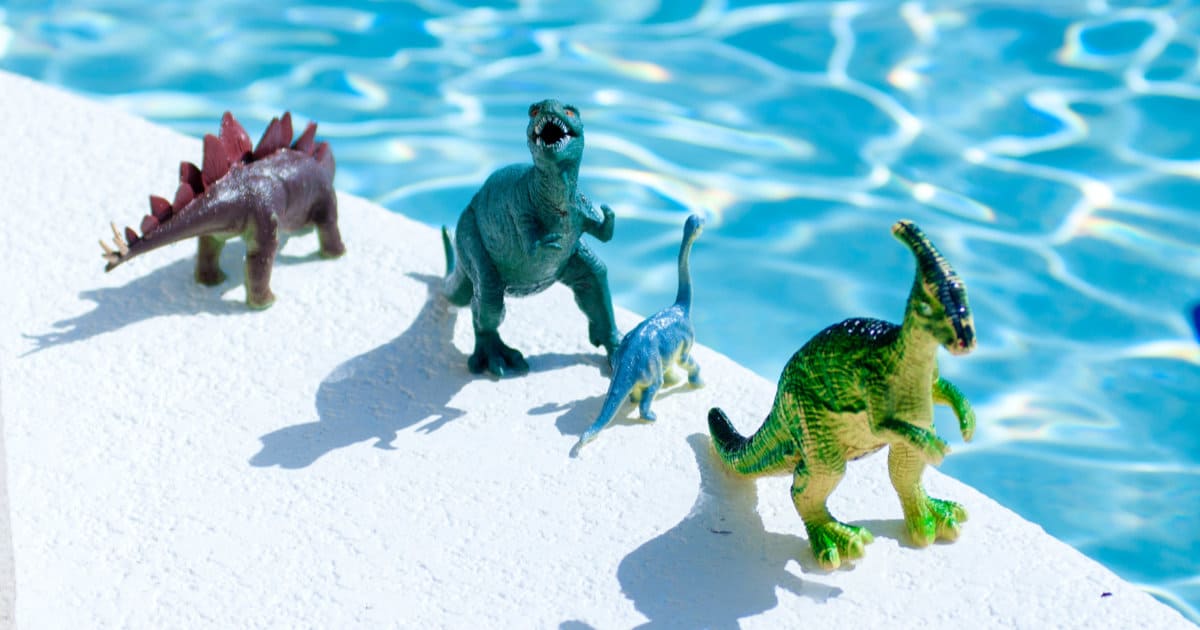 Three toy dinosaurs standing by the swimming pools edge.